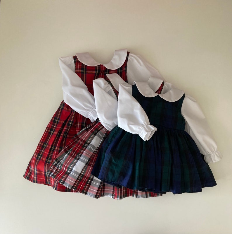 May include: Three girls' dresses with white collars and long sleeves. The dresses are made of plaid fabric in red and white, blue and white, and green and white.