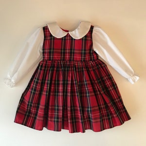 May include: A red and black plaid dress with a white Peter Pan collar and long sleeves. The dress has a full skirt and is made of a soft, comfortable fabric.