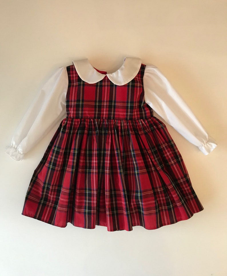 May include: A red and black plaid dress with a white Peter Pan collar and long sleeves. The dress has a full skirt and is made of a soft, comfortable fabric.