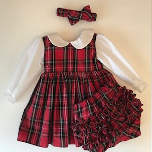 May include: A red and black plaid dress with a white Peter Pan collar and long sleeves. The dress is paired with a matching red and black plaid diaper cover with ruffles. A red and black plaid headband with a bow is included.