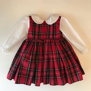 May include: A red and black plaid dress with a white Peter Pan collar and long sleeves. The dress has a gathered skirt and a back zipper.