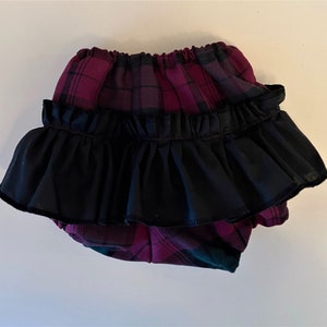 May include: Purple and black plaid baby bloomers with a black ruffle trim.