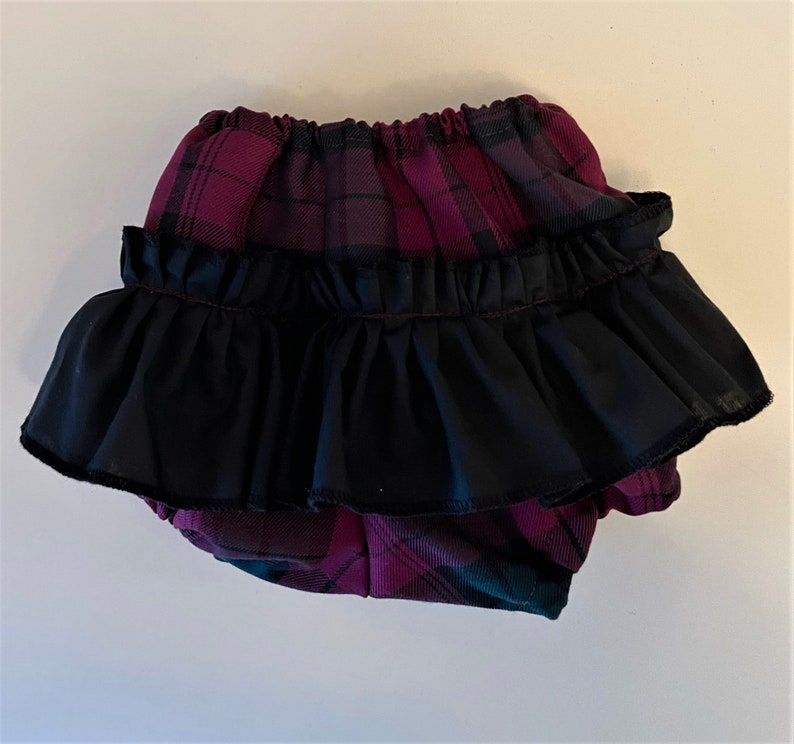 May include: Purple and black plaid baby bloomers with a black ruffle trim.