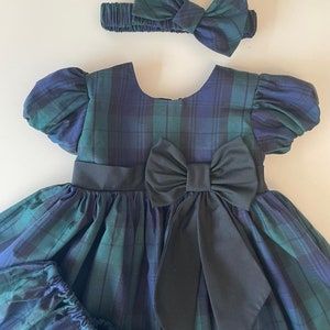 Peut inclure: Une robe &agrave; carreaux verts et bleus avec un n&oelig;ud noir et un bandeau assorti. La robe a des manches bouffantes et une jupe ample.