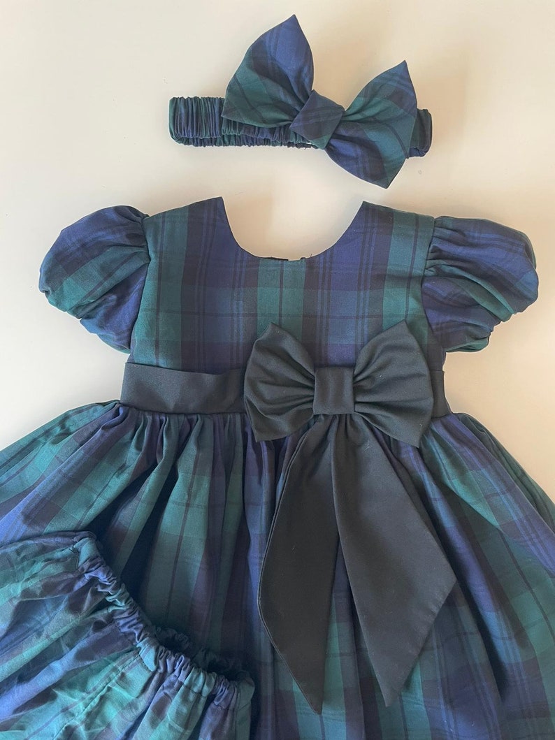 Peut inclure: Une robe &agrave; carreaux verts et bleus avec un n&oelig;ud noir et un bandeau assorti. La robe a des manches bouffantes et une jupe ample.