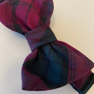 May include: A burgundy and black plaid bow tie. The bow tie is made of a soft, textured fabric.