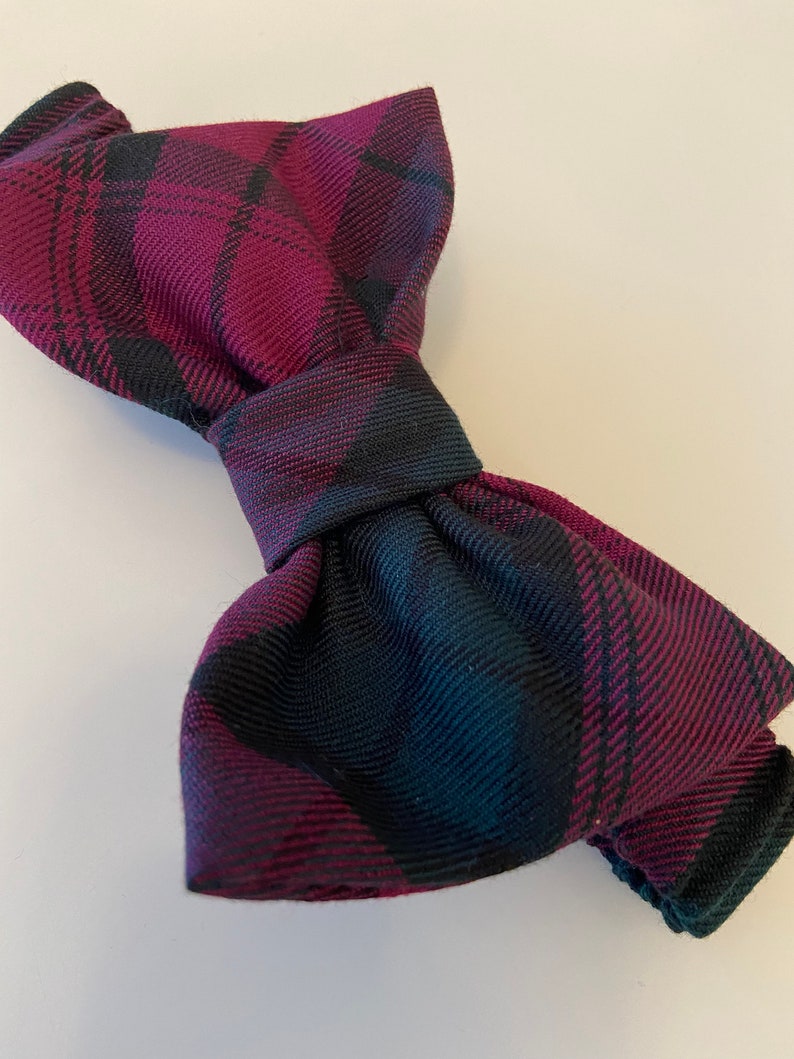 May include: A burgundy and black plaid bow tie. The bow tie is made of a soft, textured fabric.