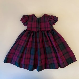 May include: A red and green plaid dress with puffed sleeves. The dress has a gathered skirt and a back zipper.