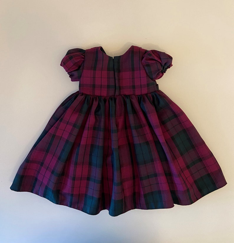 May include: A red and green plaid dress with puffed sleeves. The dress has a gathered skirt and a back zipper.