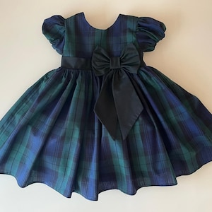 Peut inclure: Une robe &agrave; carreaux bleus et verts avec un n&oelig;ud noir. La robe a des manches bouffantes courtes et une jupe ample.