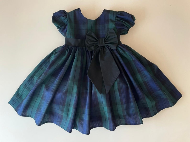 Peut inclure: Une robe &agrave; carreaux bleus et verts avec un n&oelig;ud noir. La robe a des manches bouffantes courtes et une jupe ample.