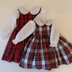 May include: Two red and white plaid dresses with white Peter Pan collars and long white sleeves. The dresses have a gathered skirt and are perfect for a holiday party.