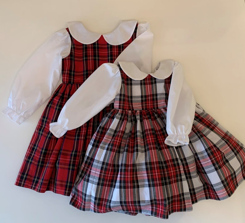 May include: Two red and white plaid dresses with white Peter Pan collars and long white sleeves. The dresses have a gathered skirt and are perfect for a holiday party.