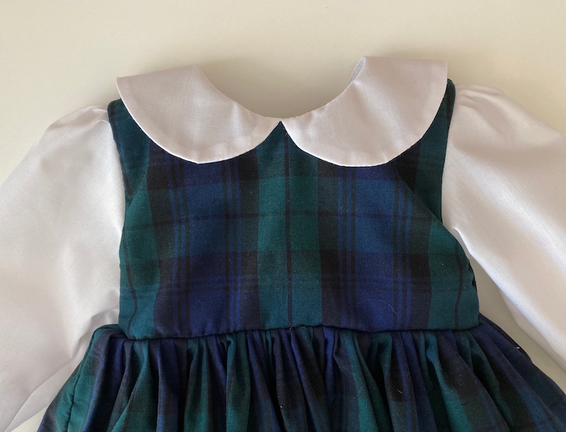 May include: A green and blue plaid dress with a white Peter Pan collar and long sleeves. The dress has a gathered skirt and is made of a soft, comfortable fabric.