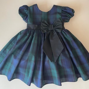 Peut inclure: Une robe &agrave; carreaux bleus et verts avec un n&oelig;ud noir. La robe a des manches bouffantes courtes et une jupe ample.
