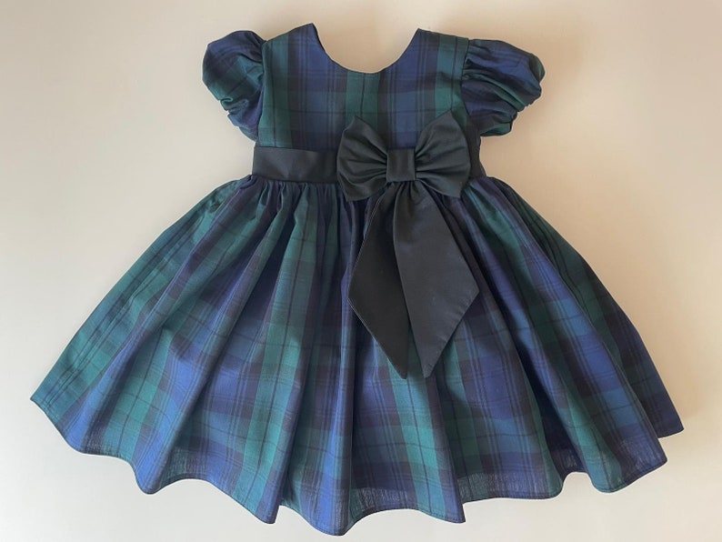 Peut inclure: Une robe &agrave; carreaux bleus et verts avec un n&oelig;ud noir. La robe a des manches bouffantes courtes et une jupe ample.