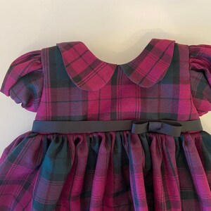 May include: A plaid dress with a black ribbon and bow. The dress has a Peter Pan collar and puffed sleeves.