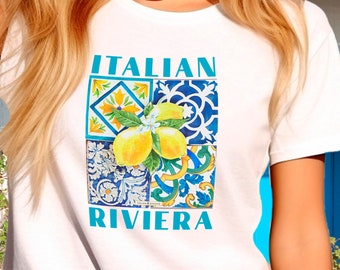May include: White t-shirt with the words "ITALIAN RIVIERA" in turquoise. The shirt features a graphic of lemons and Italian tile patterns in yellow, blue, and white. The text "ITALIAN SUMMERS" is at the bottom.