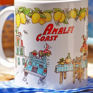 May include: White ceramic mug with a colorful illustration of a car driving through a town with the text "Amalfi Coast" and lemons on a vine. The mug is on a blue and white checkered tablecloth.