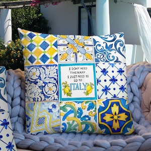 May include: A decorative pillow with a patchwork design featuring blue, yellow, and white tiles. The pillow has a quote that reads "I don't need therapy I just need to go to... ITALY".
