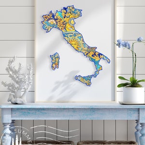 Puede incluir: Una impresión enmarcada de un mapa de Italia con un contorno azul. El mapa está lleno de un patrón colorido de flores y hojas. La impresión está colgada en una pared blanca sobre una mesa pintada de azul con dos cestas de mimbre.