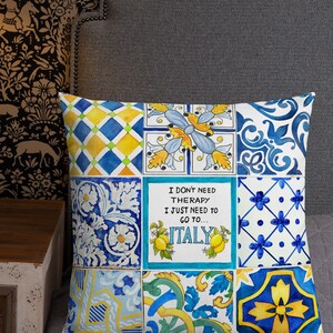 May include: A decorative pillow with a patchwork design featuring blue, yellow, and white tiles. The pillow has a quote that reads "I don't need therapy I just need to go to... ITALY".