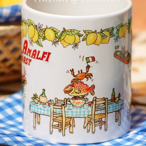May include: White ceramic mug with a colorful illustration of a table setting with a fish, crab, and lemons. The mug has the text "Amalfi Coast" and "Italian Summers" printed on it.