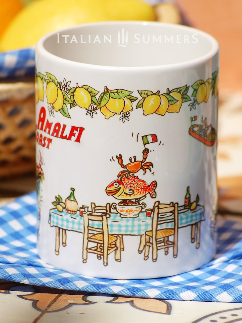 May include: White ceramic mug with a colorful illustration of a table setting with a fish, crab, and lemons. The mug has the text "Amalfi Coast" and "Italian Summers" printed on it.