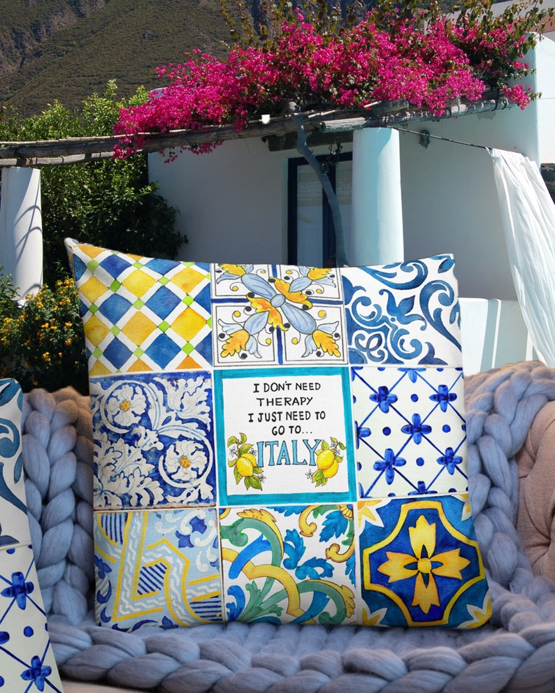 May include: A decorative pillow with a patchwork design featuring blue, yellow, and white tiles. The pillow has a quote that reads "I don't need therapy I just need to go to... ITALY".