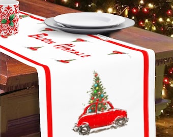 May include: White table runner with a red border. The runner features a red car with a Christmas tree on top and the words "Buon Natale" in red lettering. The runner is on a wooden table with a Christmas tree in the background.