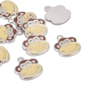 May include: A set of ten silver-toned monkey charm pendants with brown ears and a yellow face. Each charm has a loop for attaching to a necklace or bracelet.