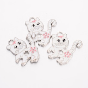 May include: Three white metal charms shaped like cats with pink accents. Each charm has a pink bow on its head and pink flowers on its body.