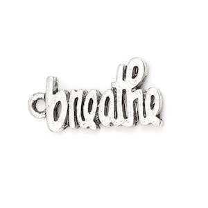 May include: A silver-colored charm with the word "breathe" in a cursive font. The charm has a loop on the left side for attaching to a necklace or bracelet. The word is in a slightly distressed style.