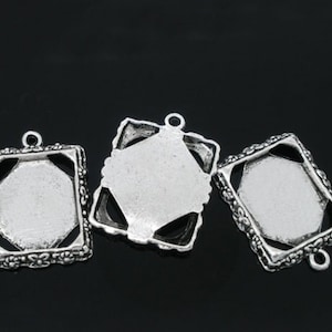 May include: Three silver-toned metal pendant trays with ornate edges. The trays are designed to hold small cabochons or other decorative elements.