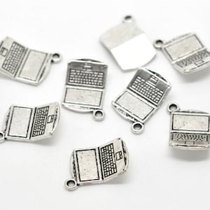 May include: A collection of silver-colored laptop charms. Each charm features a detailed keyboard and screen, with a small loop for attaching to jewelry or other crafts. The charms are scattered on a white surface.