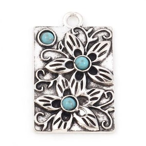 May include: A rectangular silver pendant with a floral design and three turquoise-colored stones. The pendant features two large flowers and a smaller stone at the top. The design is detailed with swirling patterns.