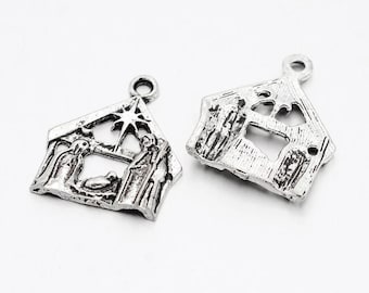 May include: Two silver-coloured metal charms shaped as a nativity scene. One charm shows the holy family with a star above. The other charm is a similar shape with a textured surface and a hole for stringing.