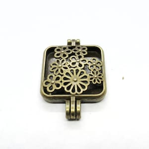 May include: A square-shaped bronze pendant with a filigree design of flowers. The pendant has a loop at the top for attaching to a chain or cord.