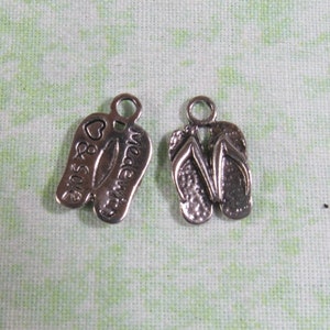 May include: Two silver charm pendants shaped like flip flops. One flip flop has the words "Made With" and a heart on it. The other flip flop has the words "& Sole" on it.