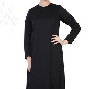 May include: A black long-sleeved maxi dress with a round neckline. The dress has a simple, elegant design and a flowing silhouette.