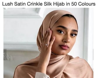 May include: A woman wearing a light brown satin hijab. The hijab has a crinkled texture and is made of silk. The hijab is draped over the woman's head and shoulders.