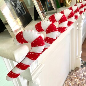 May include: A white mantelpiece decorated with red and white candy cane ornaments. The candy canes are made of felt and have a stitched design.