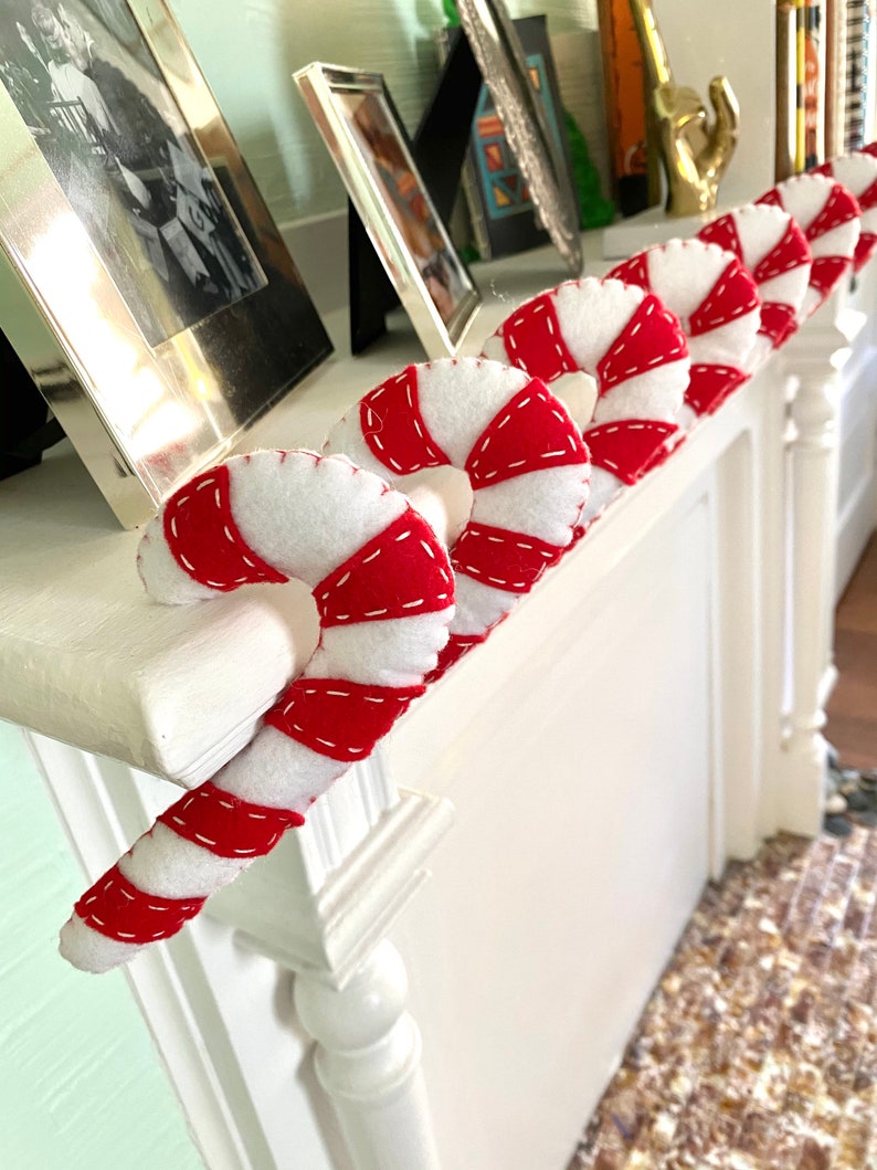 May include: A white mantelpiece decorated with red and white candy cane ornaments. The candy canes are made of felt and have a stitched design.