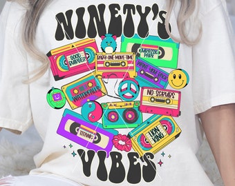 May include: A white t-shirt with a graphic design featuring the text "NINETY'S VIBES" in a retro font. The design includes a variety of colorful cassette tapes, a peace sign, and a cartoon dinosaur.