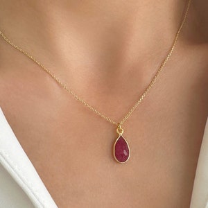 Op de afbeelding: Een gouden ketting met een traanvormige hanger met een rode edelsteen.