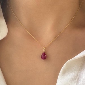 May include: A gold chain necklace with a teardrop-shaped ruby pendant.
