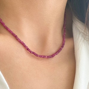 Può includere: Una collana delicata realizzata con piccole pietre preziose rosa di forma quadrata. La collana è indossata da una persona con i capelli castani.