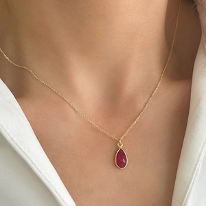 May include: A gold chain necklace with a teardrop-shaped pendant featuring a red gemstone.