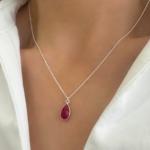 May include: A silver chain necklace with a teardrop-shaped pendant featuring a deep red gemstone.