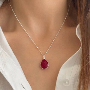 Op de afbeelding: Een zilveren ketting met een hanger in de vorm van een traan, gemaakt van een rode edelsteen.